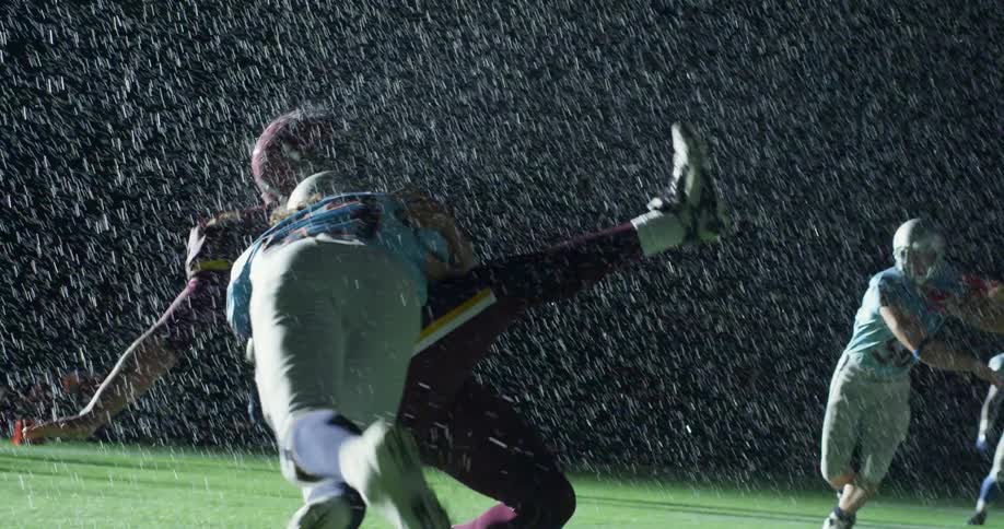 One football player tackles another in the rain