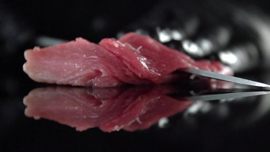 A person wearing black gloves slices a piece of meat with a knife