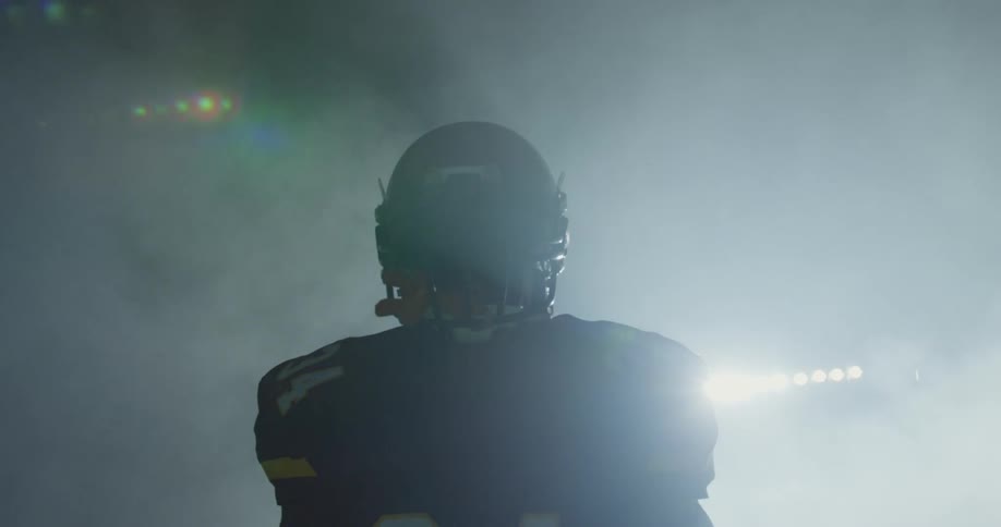 A football player walks in a stadium in full uniform at night
