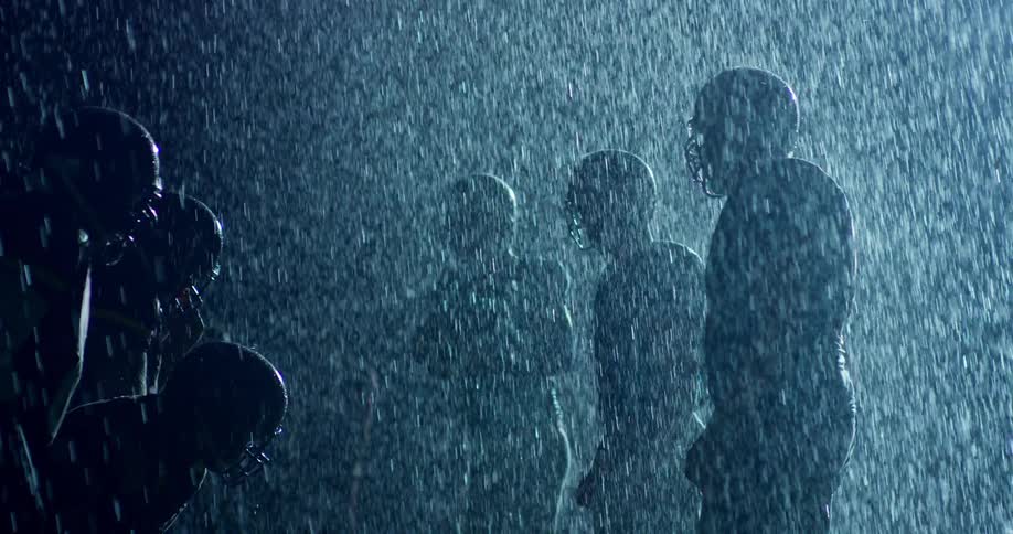 A group of football players face-off outside in the pouring rain
