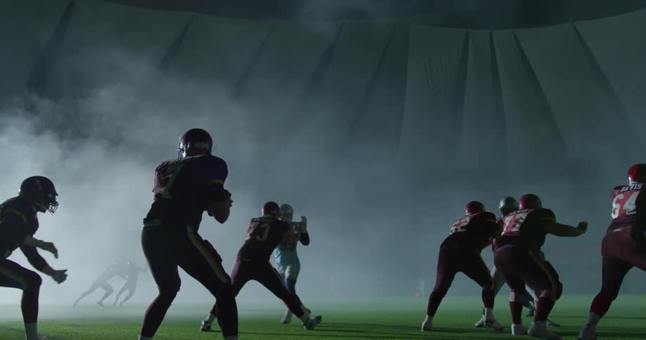 Football players all scramble for the football on the field with smoke in the dark