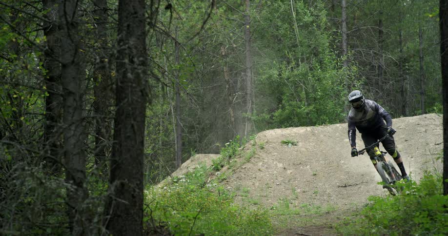 A mountain biker whips his bike sideways on a forest jump