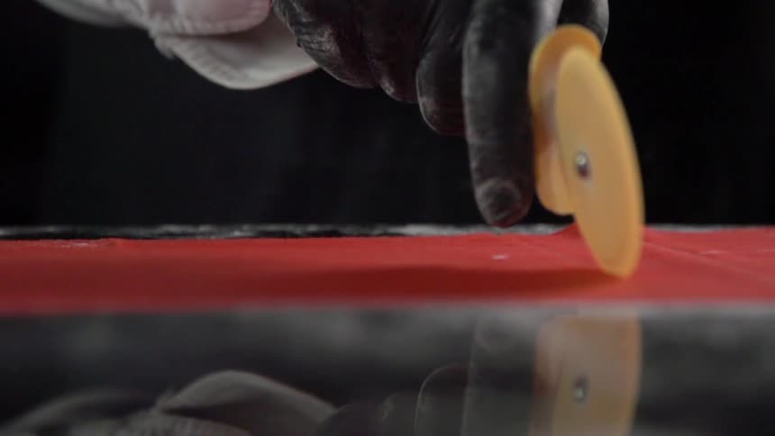 A white person uses a pizza cutter to slice a sheet of red food