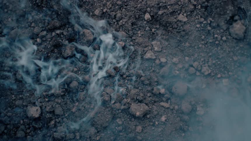 Smoke curls and rises from the rocky ground