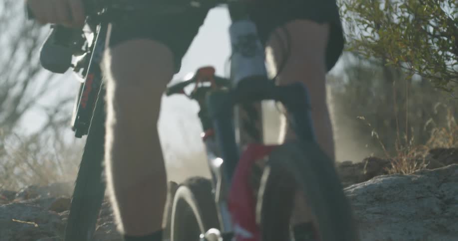 Mountain bike riders jump their bikes down a trail on a sunny day