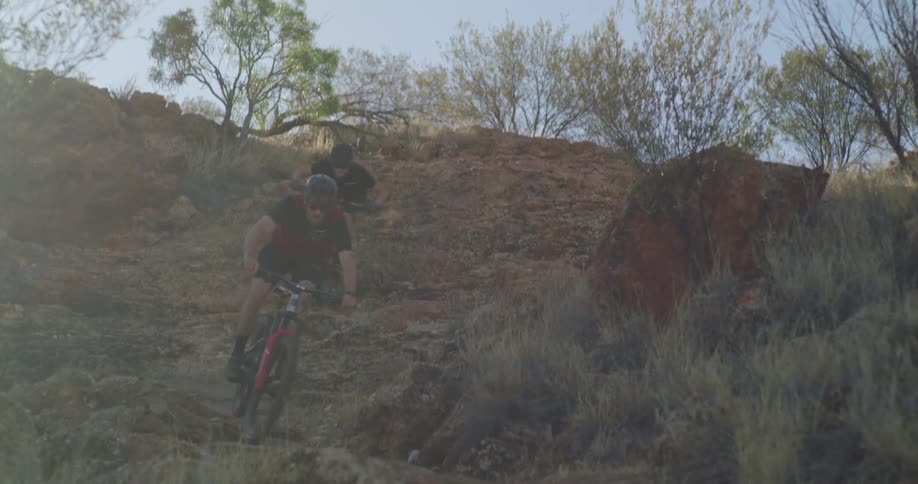 Two people cycle down a rocky hill