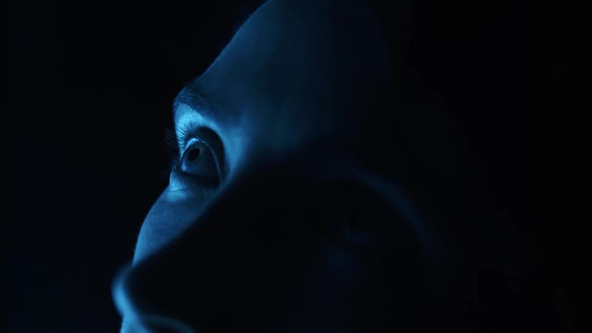 A woman stands in the darkness and looks up
