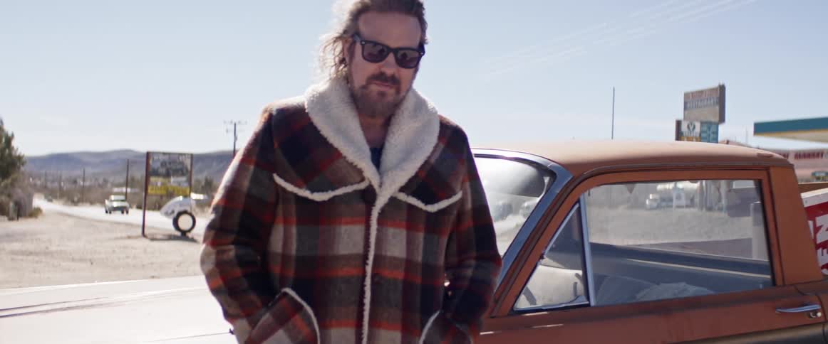 Man wearing jacket and sunglasses stands near pickup truck parked near highway