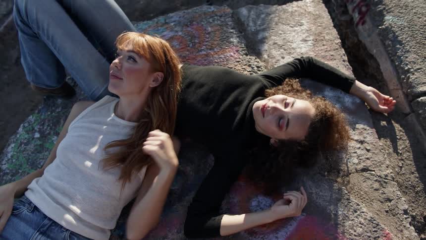 A woman lies down on a rock and then another woman lies down and rests her head on her stomach