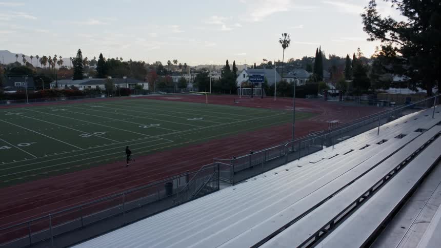 A person runs by themself along a sports field track