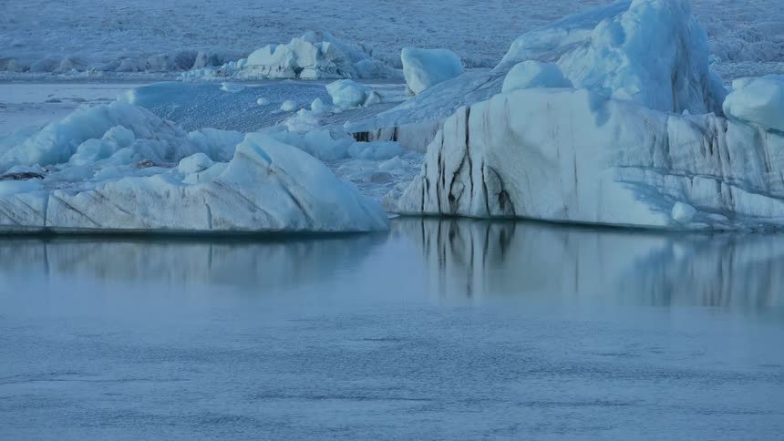 Ice bergs reflect on the surface of the water as some flows by