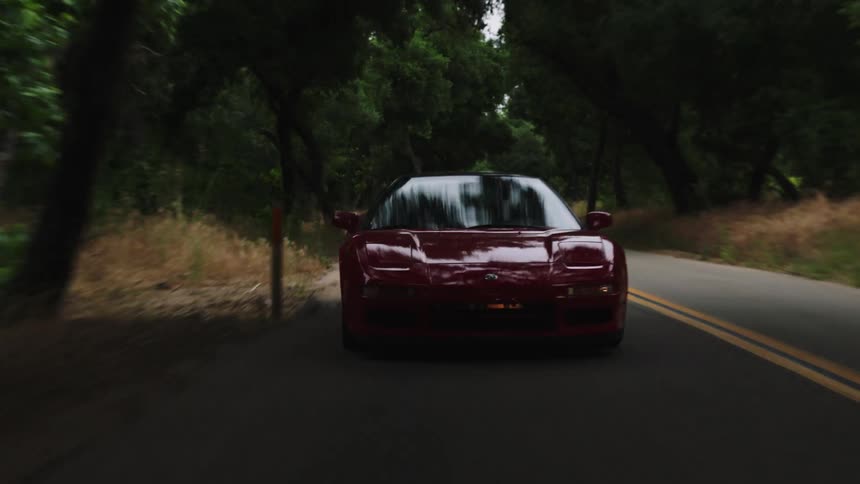 A red sports car travels on a forest road