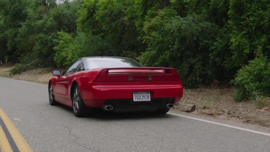 A red sports car drives down a road through a forest
