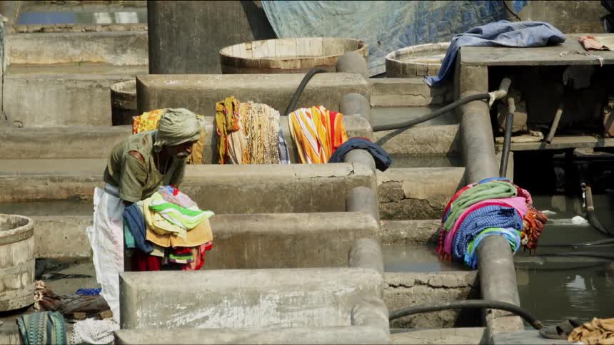 A man smacks a piece of clothing on the ground surrounded by piles of other clothing