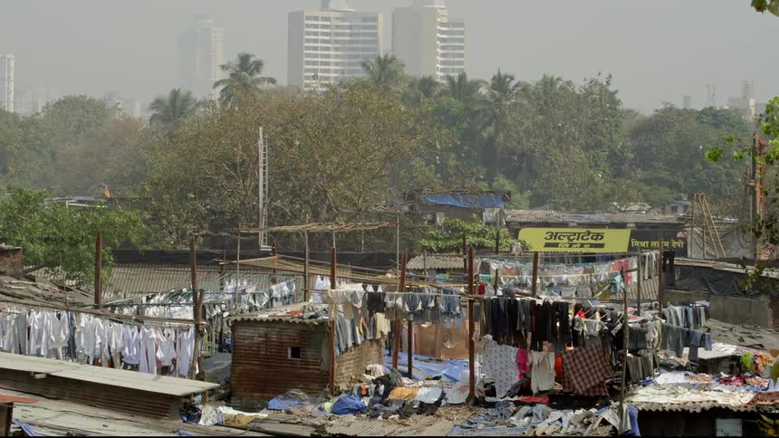 A shanty hut with clothes hanging on clotheslines with trees and the city skyline in the background