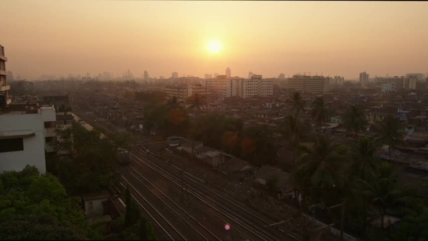 The low sun illuminating a train track in a city as a train passes through