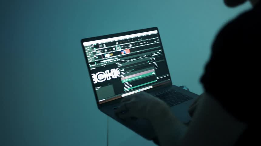 Laptop dj works on computer under strobe lights
