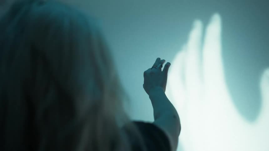 A woman reaches her had to touch a large hand projected on a wall