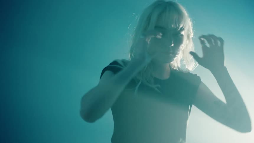 A blonde woman dressed in black stands in front of a bright projection screen