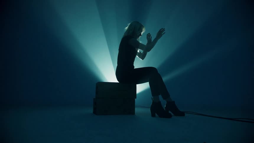 A woman sits and moves her hands against a light projected behind her