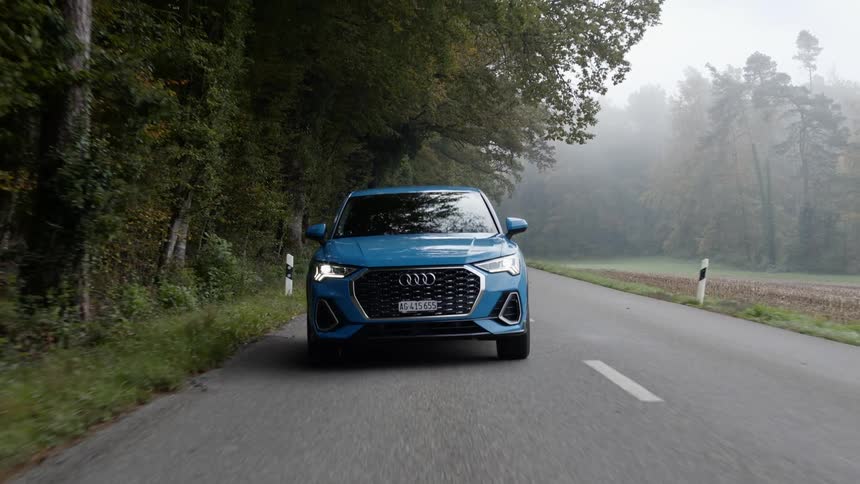 A blue car drives down a road in a forest