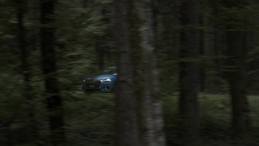 A blue car zips down a road that runs through a thick forest