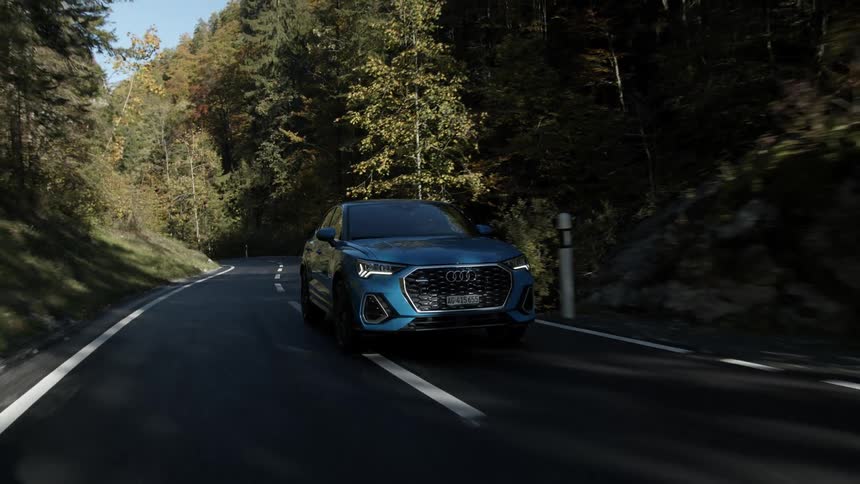 A blue audi being driven down a road through a mountain forest