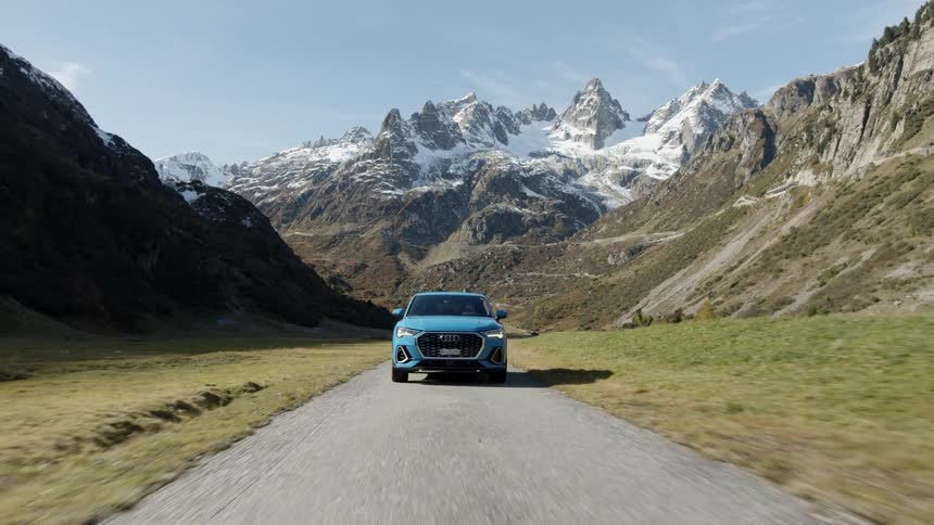 A blue car drives down a road running through a mountain valley