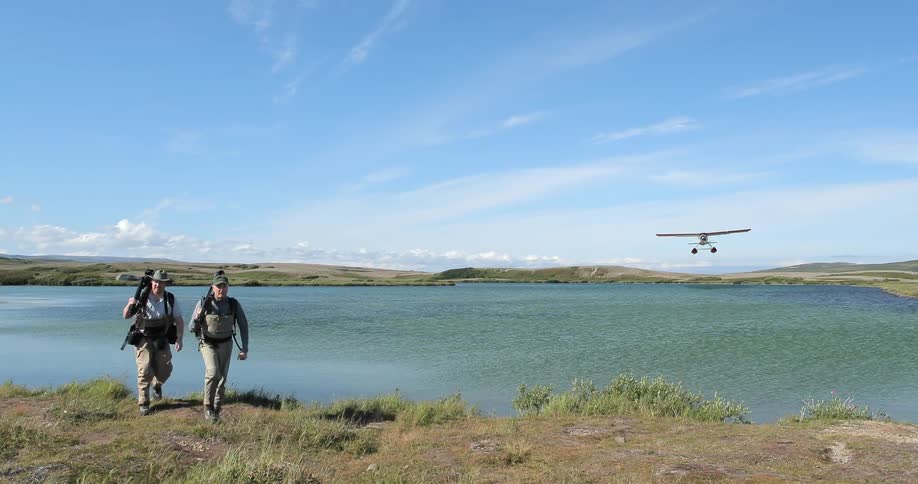 Men walking next to a body of water as a small plane passes overhead