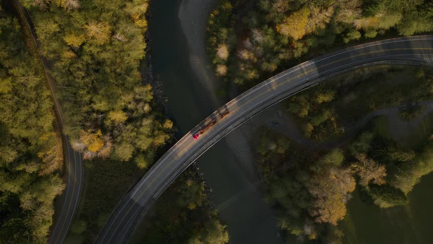 Birds eye view of a semi truck hauling cargo on a curved bridge across a river