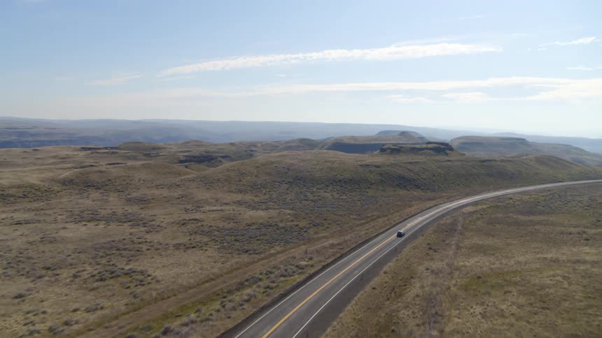 A car drives down a lonely highway in an arid landscape