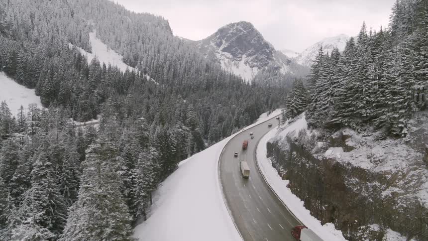 Cars and semi trucks travel on a snowy mountain highway