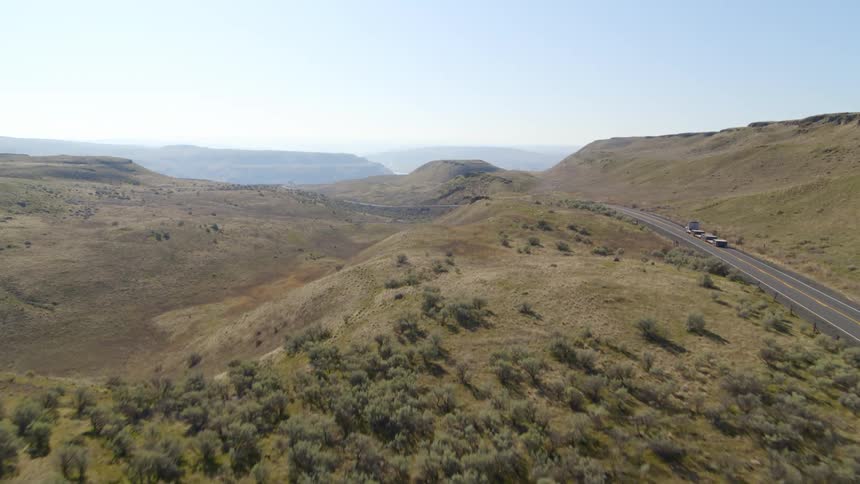 A flatbed semi truck traveling down a highway through rugged terrain