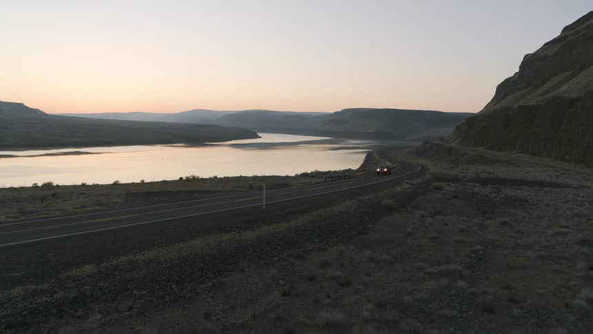A black pickup truck travels on a country road through rugged foothills at sunrise