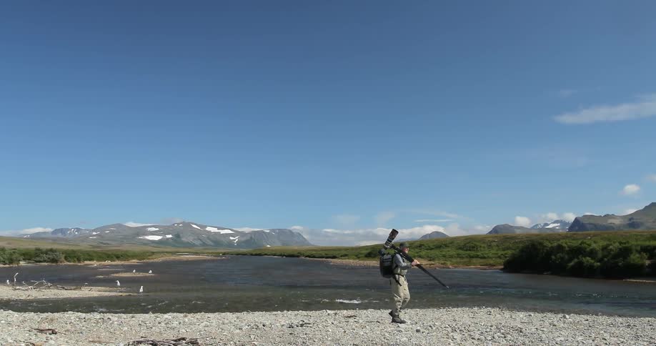 A man is walking along some rocks by the water carrying a camera