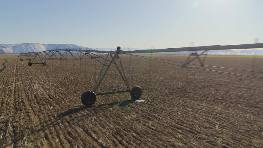 Flying along irrigation equipment on tilled farmland under a clear blue sky
