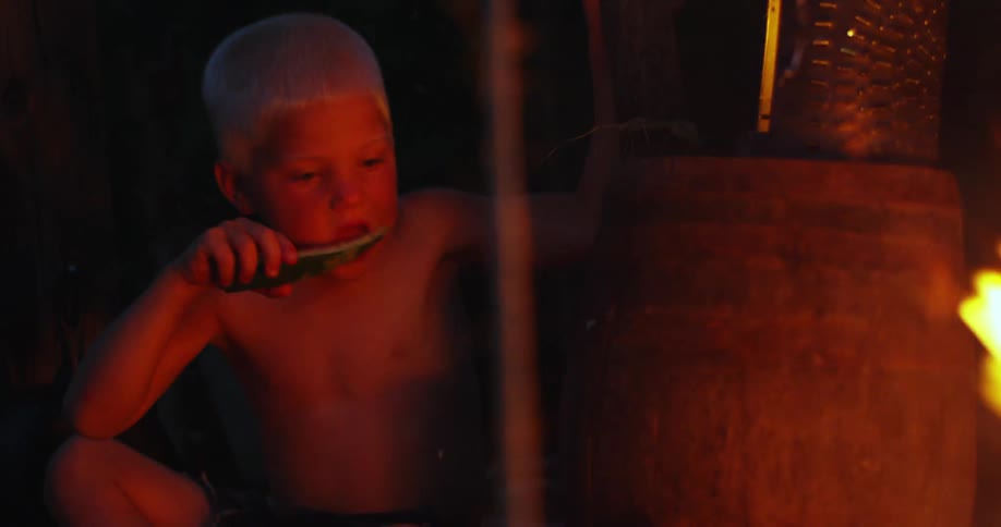 Two young white boys sit around a campfire outdoors