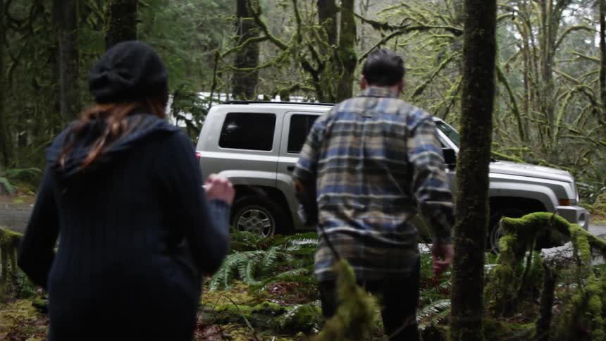 Three people walk out of a forest towards a vehicle