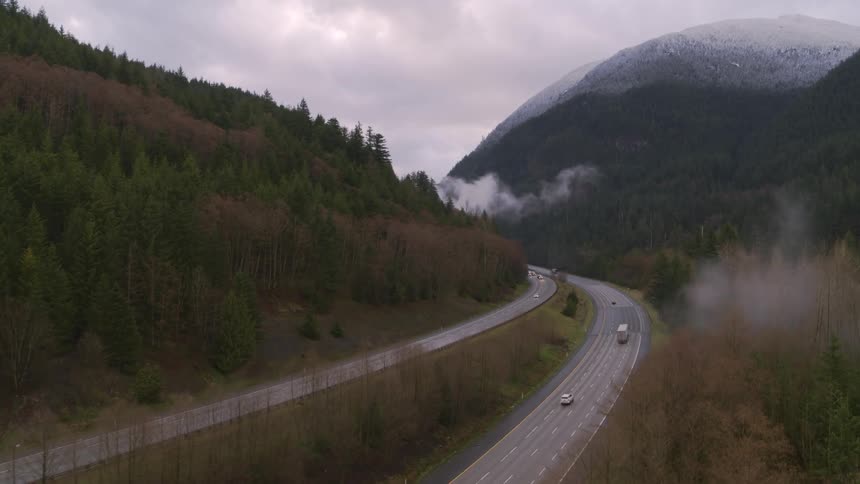 Cars and trucks drive on a curved section of mountain valley highway