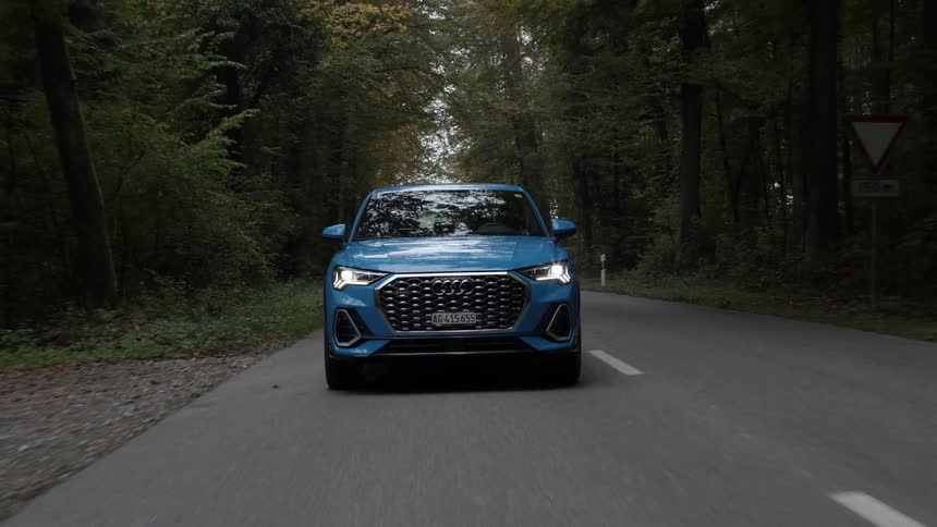 A blue vehicle drives down a road that runs through a deep forest