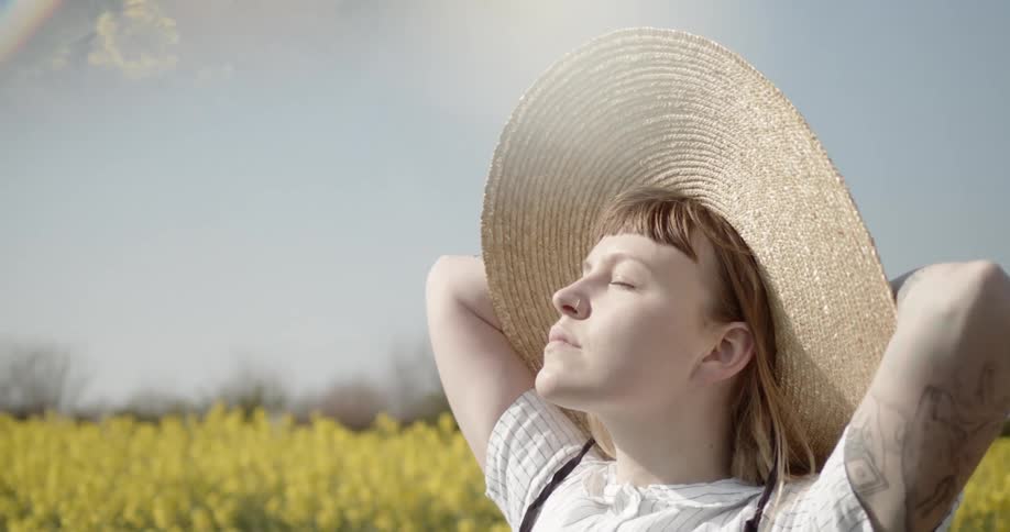 Young woman in straw hat stands in sunlight with eyes closed