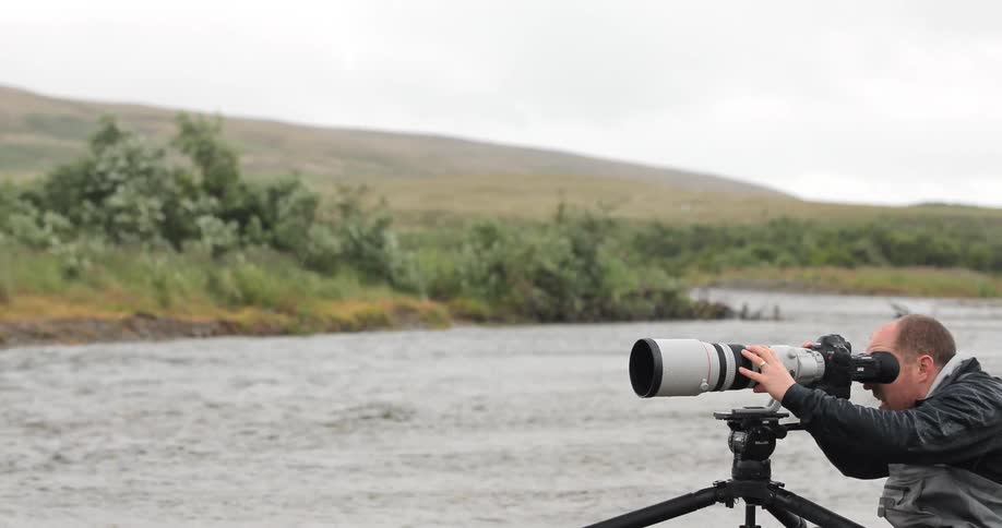 A man is using a camera on some rocks by a creek
