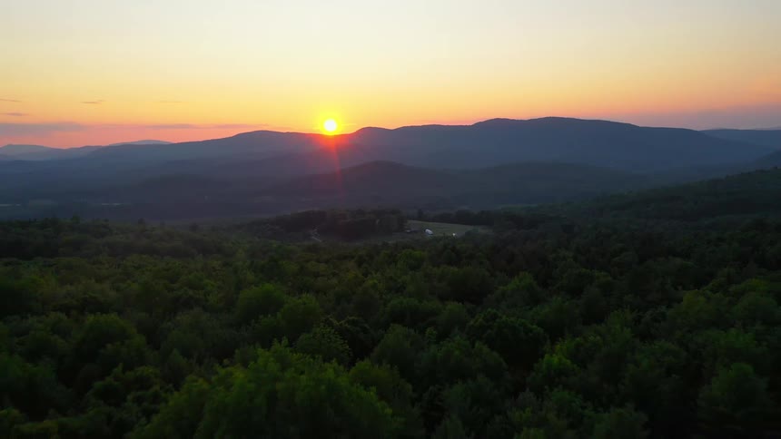 The sun sets over a vast forest near a mountain range