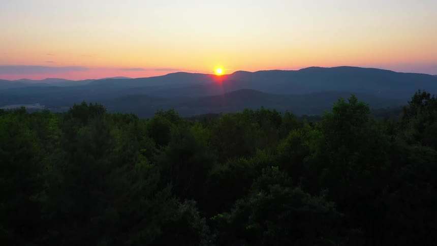 The sun rises behind the mountains near the forest