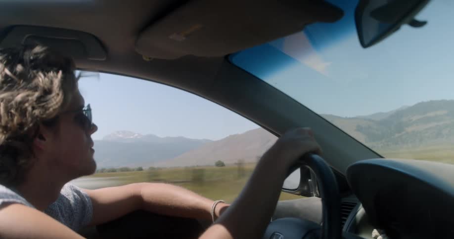 A white male with sunglasses drives a car down a road