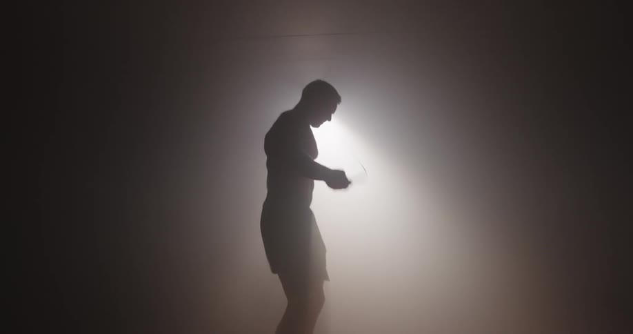 A man is jumping rope in the dark foggy room