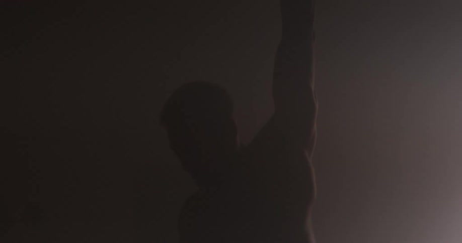 Silhouette of a strong muscular man lifting a dumbbell in a dimly lit room