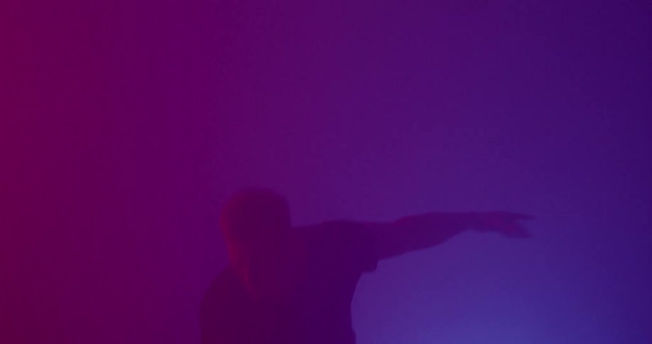 A man exercising with a kettlebell in a dark room illuminated by violet and purple lights