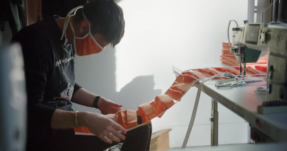 A white teenager examines orange pieces of fabrics in a room with a sewing machine