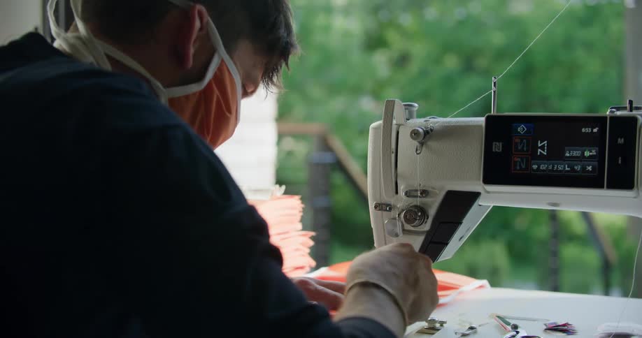 A white teenage male sews fabric with a sewing machine